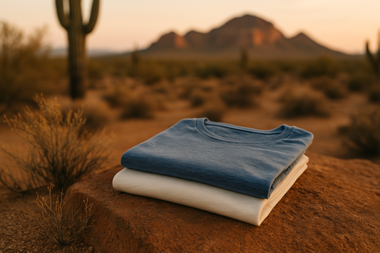 Stack of organic cotton and recycled polyester blend t-shirts in Arizona desert landscape with mountains and cactus at sunset.
