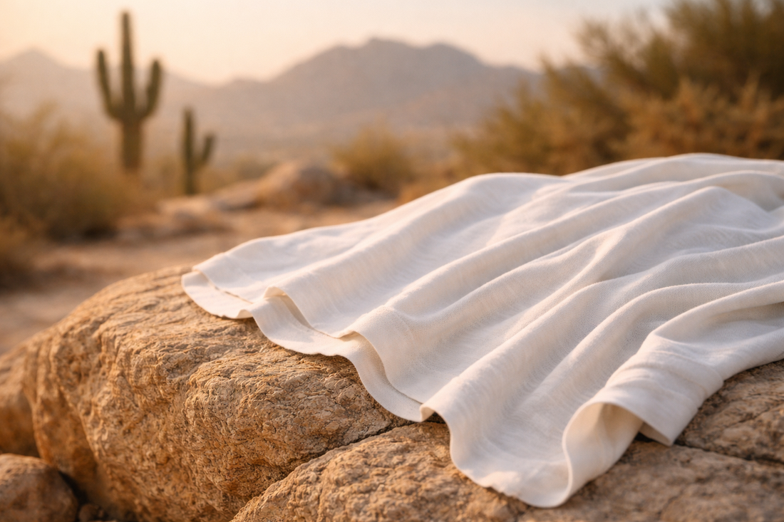 White organic cotton T-shirt draped over sunlit desert rock in Arizona, highlighting breathable fabric texture with saguaro cacti and mountains softly blurred in the background.
