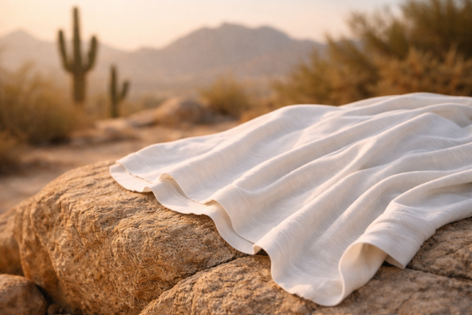 White organic cotton T-shirt draped over sunlit desert rock in Arizona, highlighting breathable fabric texture with saguaro cacti and mountains softly blurred in the background.